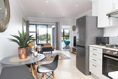 a kitchen and living room with a table and chairs at 6 Atlantic Port - Cosy, modern 2-bedroom apartment - Blouberg in Bloubergstrand