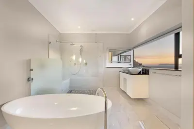a white bathroom with a tub and a window at Zaria Sun Penthouse in Cape Town