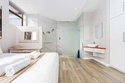 a white bedroom with a white bed and a bathroom at Zaria Sun Family in Cape Town