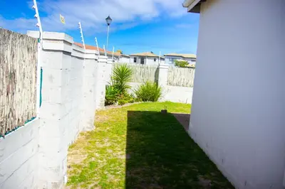 a backyard with a white brick wall and grass at Wilcre's blouberg home in Cape Town