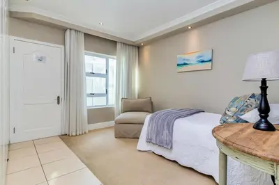 a bedroom with a bed and a table and a chair at Hermanus Beachfront Lodge - Solar Power in Hermanus