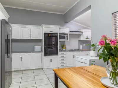 a kitchen with white cabinets and a wooden table at Hoogwater Family House in Wolseley