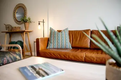a brown leather couch in a living room with a table at Milas Place Spacious & Comfortable at Bayview in Hermanus