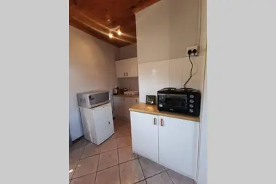 a small kitchen with white cabinets and a microwave at Cozy, peaceful garden cottage in Cape Town