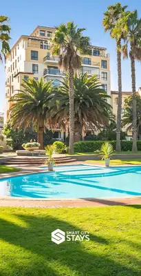 a swimming pool with palm trees in front of a building at Island Club by Smart City Stays in Cape Town
