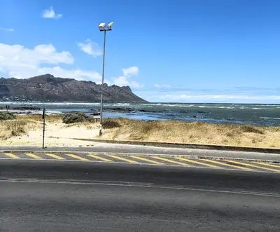 an empty road next to the ocean with a street light at Tranquil Impulse on Strand in Cape Town