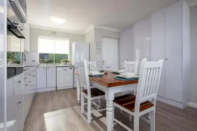 a white kitchen with a wooden table and chairs at 29@Whale Rock Estate in Hermanus