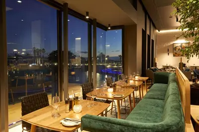 a restaurant with tables and green couches and windows at Century City Hotel Bridgewater in Cape Town