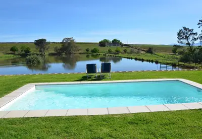 a swimming pool with two chairs in front of a lake at Under Oaks Guesthouse in Paarl