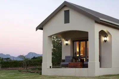 a small white house with a porch with mountains in the background at Under Oaks Guesthouse in Paarl