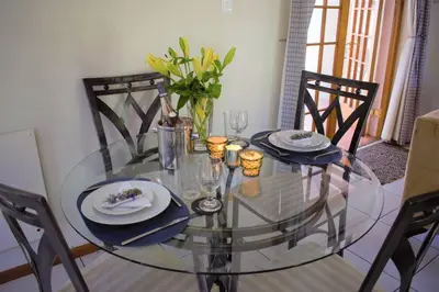 a glass dining room table with two chairs and a vase with flowers at Smith Cottage in Franschhoek