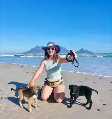 a woman kneeling on the beach with two dogs at Sunset Beach holiday accommodation in Cape Town