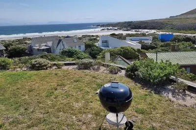 a grill sitting on top of a field next to the ocean at Hilltop Heaven, Walk to beach, Pool, Ocean & River views in Pringle Bay
