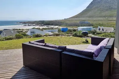 a balcony with a couch on a deck with a view of the ocean at Hilltop Heaven, Walk to beach, Pool, Ocean & River views in Pringle Bay