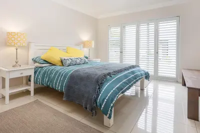 a white bedroom with a bed and a desk and windows at Tuis en Tevrede - 2 Bedroom Flat in Hermanus