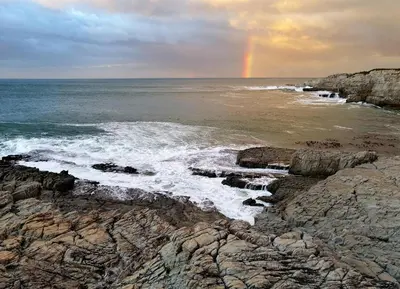 a rainbow in the sky over the ocean with rocks at Tuis en Tevrede - 2 Bedroom Flat in Hermanus
