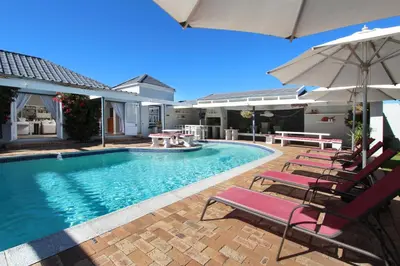 a swimming pool with chairs and an umbrella at 19th Hole Guest Lodge - Golfers paradise in Hermanus