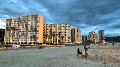 a group of people standing on a beach with a building at Ocean-Song in Strand