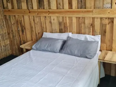 a bed with white sheets and pillows in a wooden room at Sunset beach backpackers in Bloubergstrand