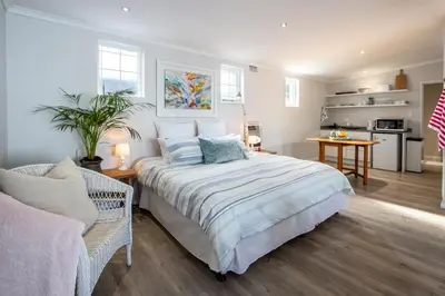a bedroom with a large bed and a kitchen at Goozi Garden Cottage in Hermanus