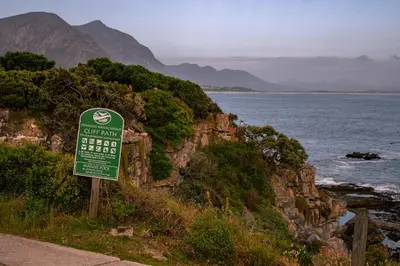 a green sign on a cliff near the ocean at Goozi Garden Cottage in Hermanus