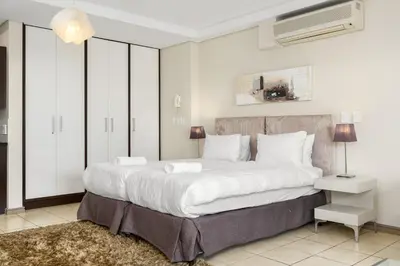 a bedroom with a large white bed and a tv at The Manhattan Apartments in Cape Town