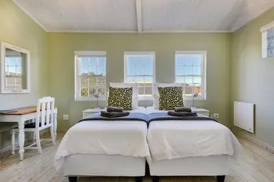 a bedroom with two beds and a desk and windows at Villa Garda B&B in Cape Town