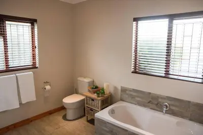 a bathroom with a tub and a toilet and windows at Sol Montis Guest Cottage in Paarl