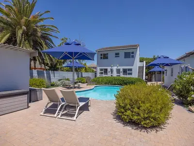 a patio with chairs and umbrellas next to a pool at Southeaster in Bloubergstrand
