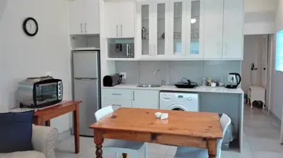 a kitchen with white cabinets and a wooden table at Seashell Cottage in Hermanus