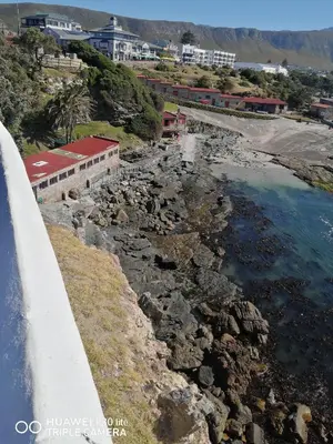 a building on a cliff next to a body of water at Seashell Cottage in Hermanus