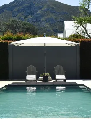 a swimming pool with two chairs and an umbrella at Fernkloof Cottage in Hermanus