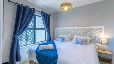 a bedroom with a bed with blue curtains and a window at Shore2Please in Cape Town