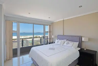 a bedroom with a bed with a view of the ocean at Nautica 2 Bedroom Beachfront Apartment with Sea Views in Bloubergstrand
