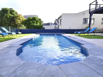 a swimming pool with blue chairs in a yard at 82 Steps to the Beach in Pringle Bay