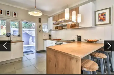 a kitchen with white cabinets and a wooden island with stools at In die Hoekie in Hermanus