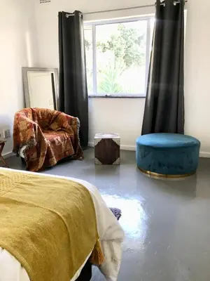 a bedroom with a bed and a chair and a window at Bird Song Cottage - Table View in Cape Town