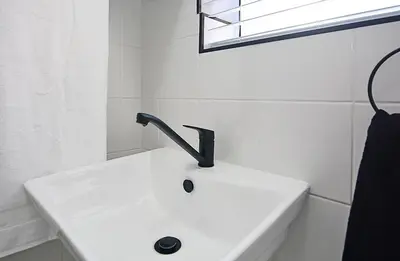a white sink with a black faucet in a bathroom at Marbella - Cozy studio in Heart of Table View in Cape Town