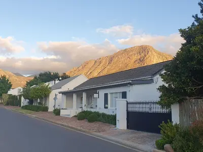 a white house on a street with mountains in the background at Petit Ermitage in Franschhoek
