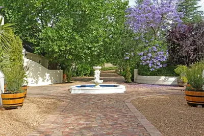 a fountain in a garden with trees and purple flowers at Kleinbosch Lodge in Stellenbosch