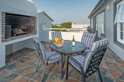 a patio with a table and chairs and a bottle of wine at Mountain View by Top Destinations Rentals in Hermanus