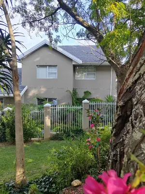 a white house with a fence and flowers at Leafy Retreat Kenridge in Durbanville