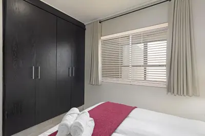 a bedroom with a bed with black cabinets and a window at Lagoon Beach 302A in Cape Town