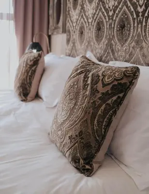a pillow on top of a bed with white sheets at Heritage Square Apartments in Durbanville