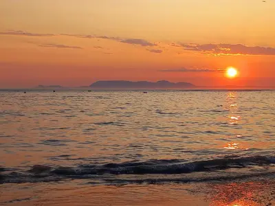 a sunset on the beach with the sun setting at Cozy Strand Beach Getaway - Studio Apartment in Cape Town