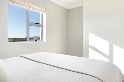 a white bedroom with a bed and a window at Stunning, Luxurious Apartment close to the beach in Cape Town