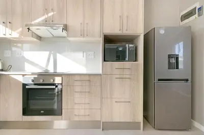 a kitchen with wooden cabinets and a stainless steel refrigerator at Stunning, Luxurious Apartment close to the beach in Cape Town