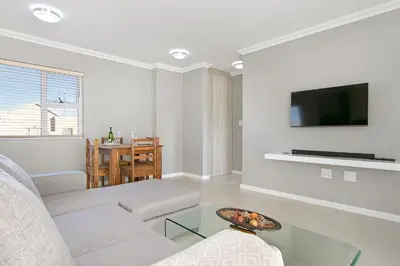 a living room with a couch and a tv on a wall at Stunning, Luxurious Apartment close to the beach in Cape Town