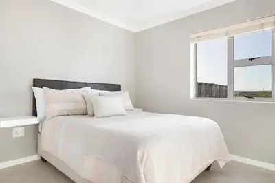 a white bedroom with a white bed with a window at Stunning, Luxurious Apartment close to the beach in Cape Town