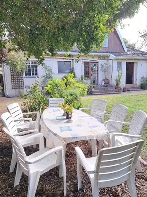 a white table with white chairs and flowers on it at Home On Uitvlugt - Peaceful leafy garden flat with sunny lounge in Cape Town